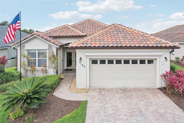 mediterranean / spanish house featuring a garage, a tiled roof, decorative driveway, and stucco siding