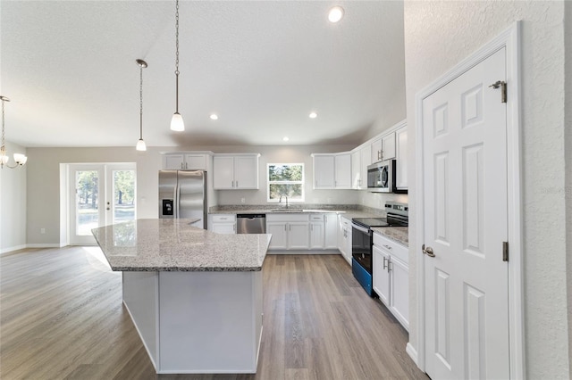 kitchen with white cabinets, light wood-style flooring, a kitchen island, hanging light fixtures, and stainless steel appliances