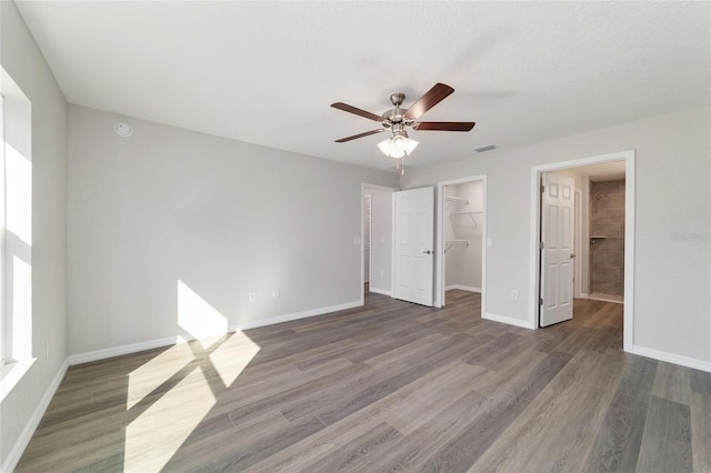 unfurnished bedroom featuring a walk in closet, dark wood-style flooring, a closet, a ceiling fan, and baseboards