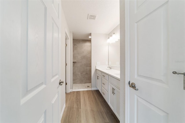 full bath with double vanity, visible vents, wood finished floors, a textured ceiling, and a shower stall