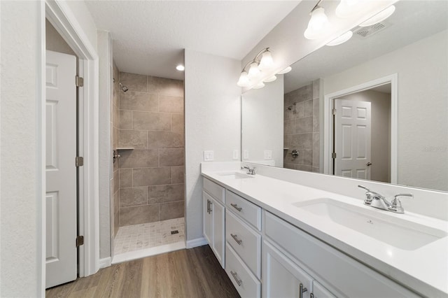 bathroom featuring double vanity, visible vents, a sink, a tile shower, and wood finished floors