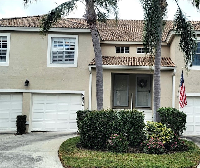 multi unit property featuring a garage, a tile roof, driveway, and stucco siding