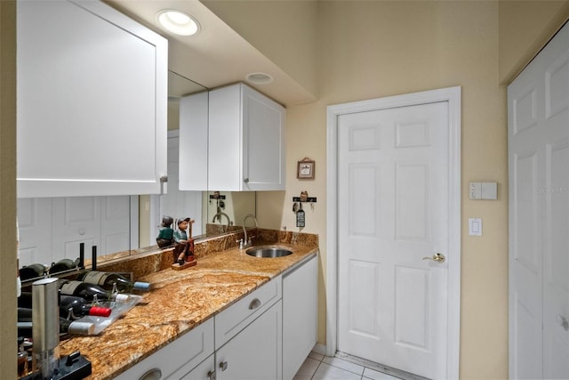 kitchen with light tile patterned flooring, a sink, light stone countertops, and white cabinets