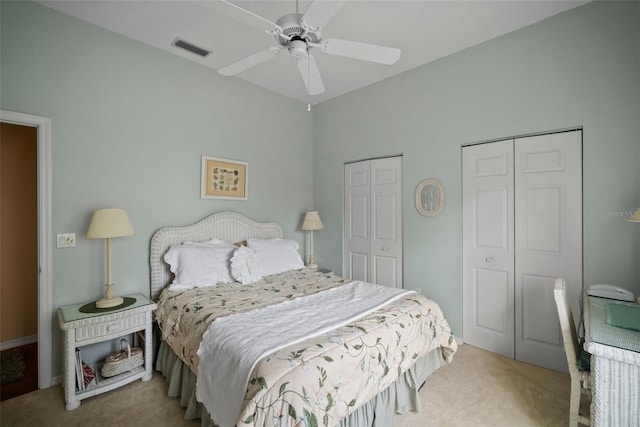 bedroom with multiple closets, visible vents, ceiling fan, and light carpet