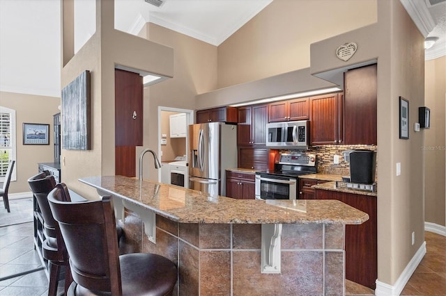 6211 90th Avenue Cir E, Parrish, FL 34219 - kitchen featuring appliances with stainless steel finishes, ornamental molding, a kitchen bar, light stone counters, and a peninsula