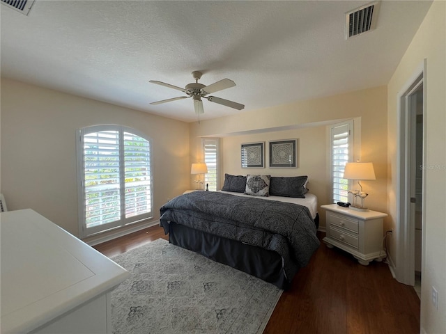 bedroom with a ceiling fan, a textured ceiling, visible vents, and dark wood-type flooring