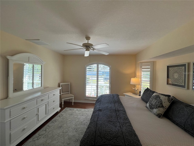 bedroom with baseboards, visible vents, dark wood finished floors, ceiling fan, and a textured ceiling