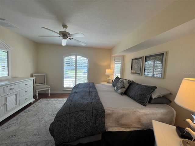 bedroom featuring multiple windows, ceiling fan, a textured ceiling, and wood finished floors