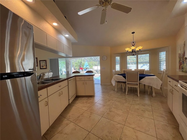 kitchen with dark countertops, freestanding refrigerator, a peninsula, white dishwasher, and a sink