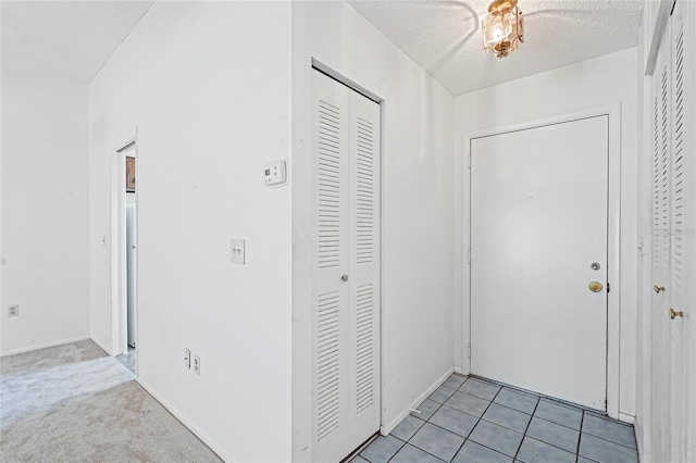 hallway with light tile patterned floors, baseboards, a textured ceiling, and light colored carpet