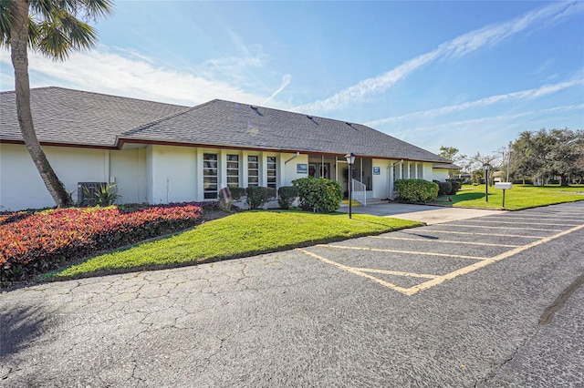 single story home featuring a shingled roof, uncovered parking, a front lawn, and stucco siding