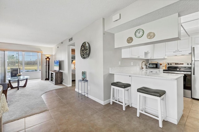 kitchen featuring light colored carpet, visible vents, freestanding refrigerator, stainless steel range with electric stovetop, and under cabinet range hood