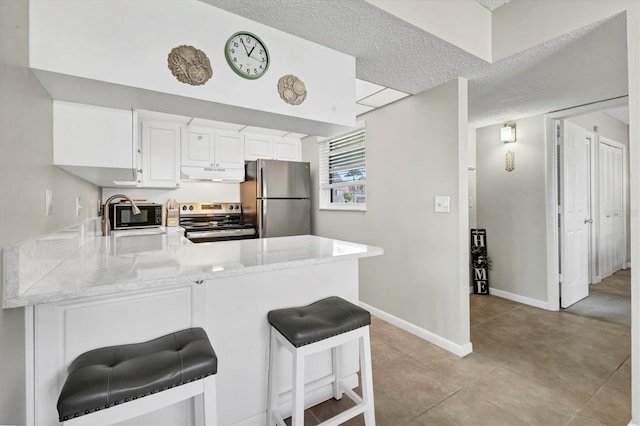 kitchen with under cabinet range hood, stainless steel appliances, a peninsula, a sink, and a kitchen breakfast bar