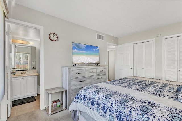 bedroom featuring visible vents, connected bathroom, light carpet, and two closets