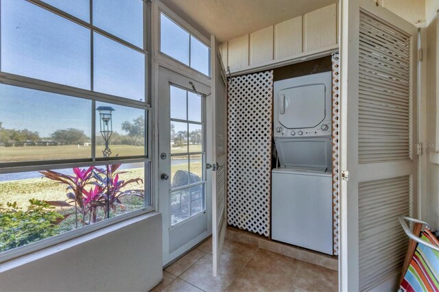 laundry room featuring stacked washer and dryer, plenty of natural light, light tile patterned floors, and laundry area