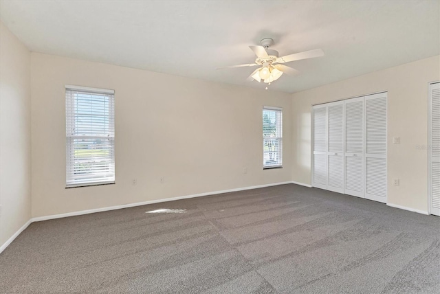 unfurnished bedroom with a ceiling fan, dark colored carpet, baseboards, and two closets