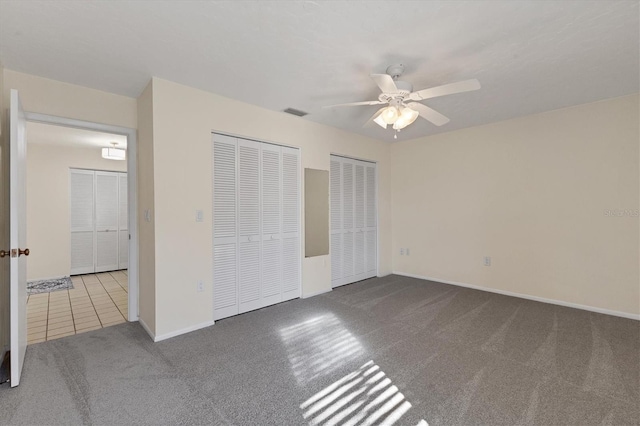 unfurnished bedroom with multiple closets, visible vents, carpet flooring, ceiling fan, and baseboards