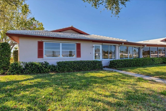 view of front of property featuring stucco siding, a tile roof, a sunroom, and a front yard