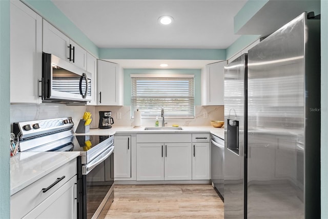 kitchen featuring light countertops, decorative backsplash, appliances with stainless steel finishes, white cabinetry, and a sink