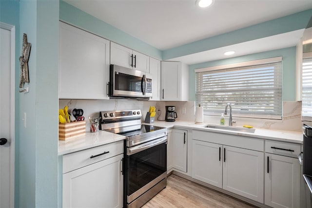 kitchen with a sink, light wood-style floors, white cabinets, appliances with stainless steel finishes, and decorative backsplash