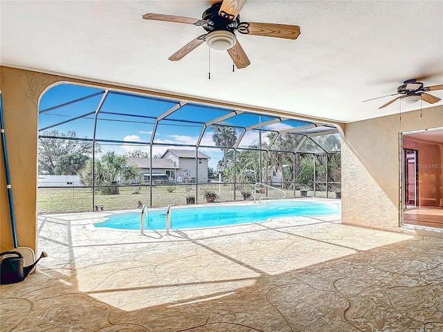 outdoor pool with glass enclosure, a patio, and a ceiling fan