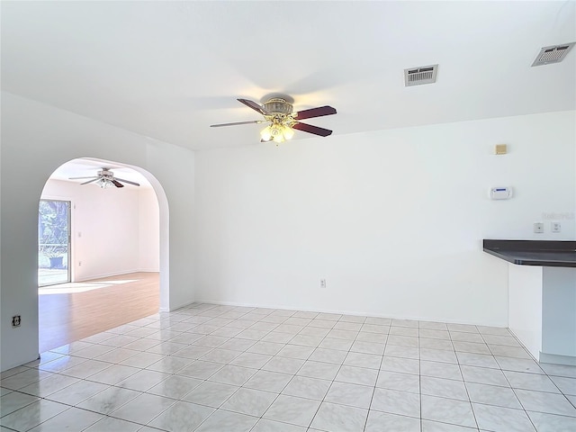 empty room featuring light tile patterned floors, visible vents, arched walkways, and a ceiling fan