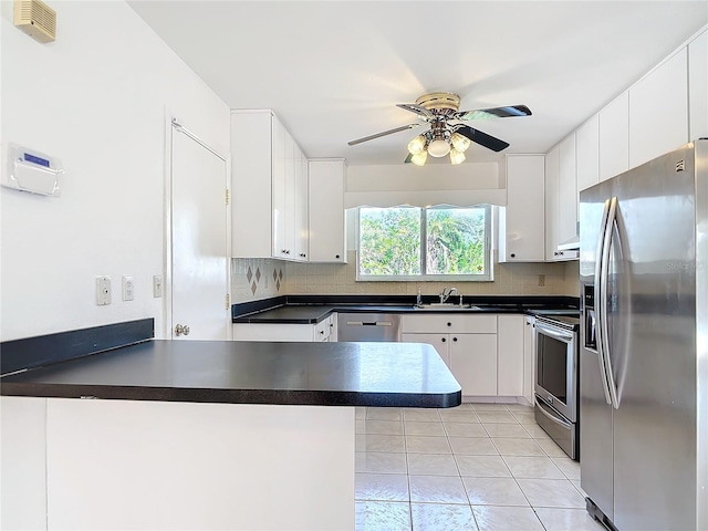 kitchen featuring dark countertops, stainless steel appliances, a peninsula, and white cabinets