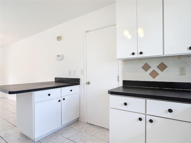 kitchen with light tile patterned floors, decorative backsplash, dark countertops, a peninsula, and white cabinetry