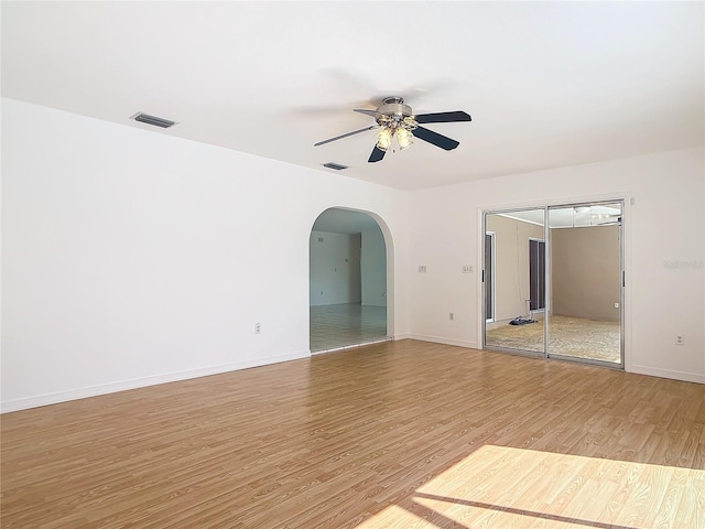 spare room featuring baseboards, visible vents, arched walkways, ceiling fan, and wood finished floors