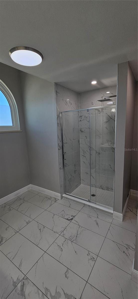 full bath featuring marble finish floor, a marble finish shower, baseboards, and a textured ceiling