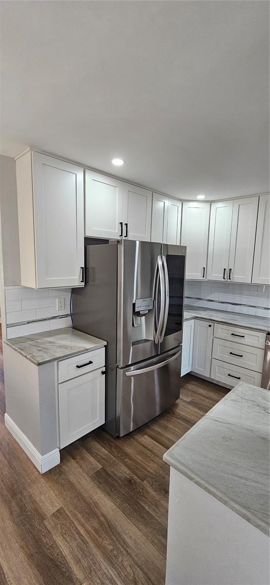 kitchen featuring decorative backsplash, dark wood-type flooring, white cabinets, light stone countertops, and stainless steel fridge with ice dispenser