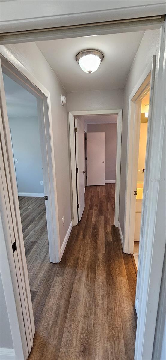 hallway featuring dark wood-style flooring and baseboards