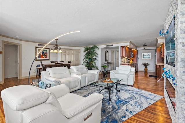 living room with a notable chandelier, wood finished floors, visible vents, baseboards, and crown molding