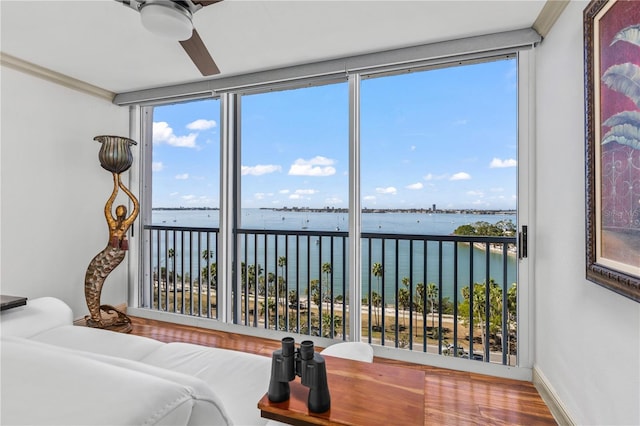 bedroom featuring baseboards, a water view, floor to ceiling windows, wood finished floors, and a ceiling fan