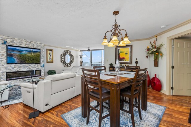 dining room with ceiling fan, a stone fireplace, wood finished floors, and crown molding