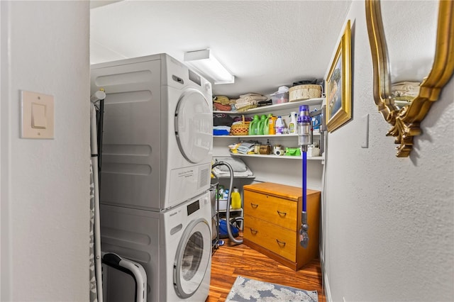 laundry area featuring a textured ceiling, a textured wall, laundry area, wood finished floors, and stacked washing maching and dryer