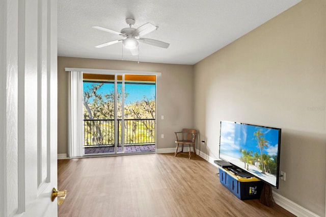 unfurnished living room with ceiling fan, a textured ceiling, baseboards, and wood finished floors