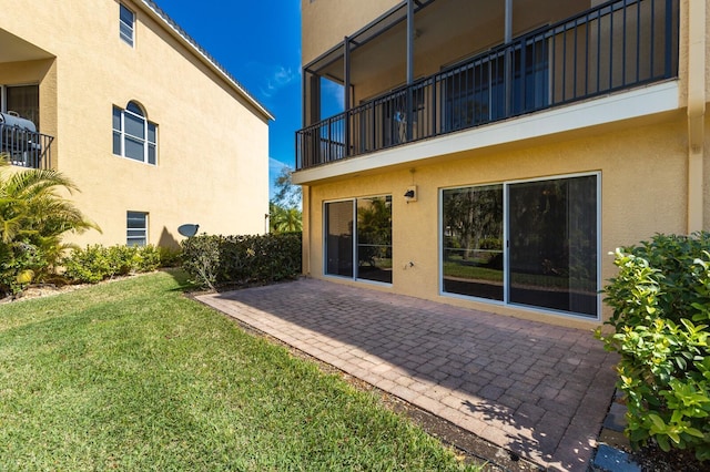 rear view of property featuring a patio, a lawn, a balcony, and stucco siding