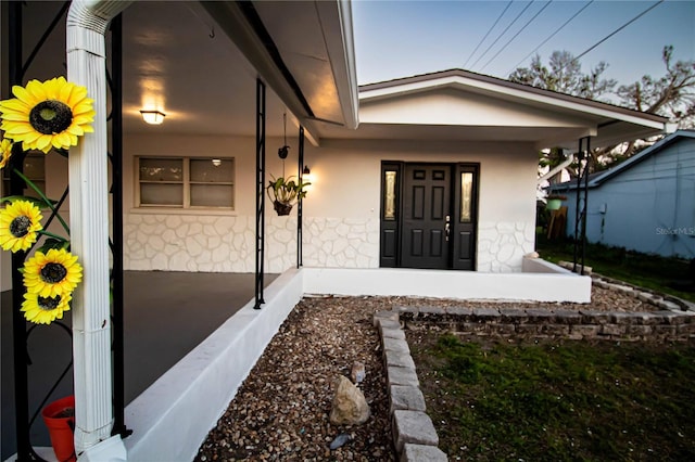 view of exterior entry featuring stone siding, a porch, and stucco siding