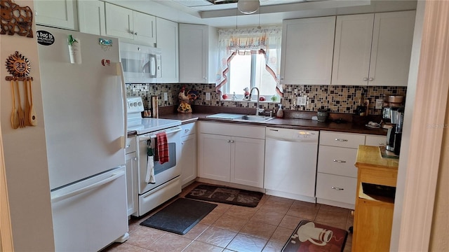 kitchen with white appliances, dark countertops, a sink, and white cabinetry