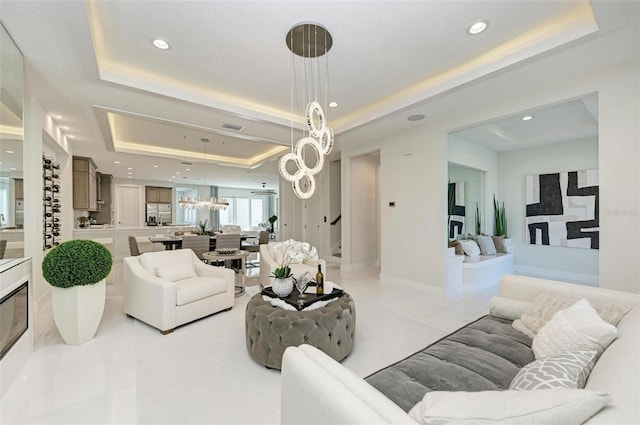 living area with light tile patterned floors, baseboards, stairway, a tray ceiling, and a notable chandelier