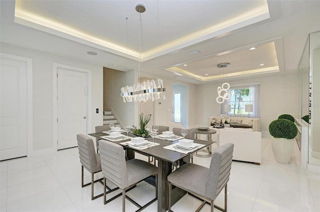 dining space featuring a raised ceiling, light tile patterned floors, a notable chandelier, and stairs