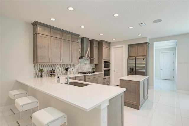 kitchen featuring stainless steel appliances, light countertops, a sink, wall chimney range hood, and a peninsula