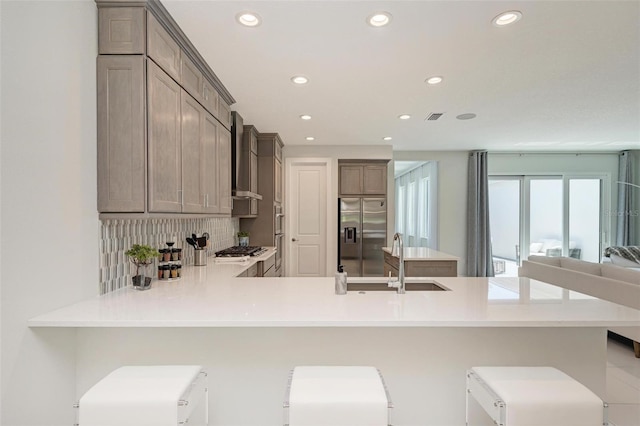 kitchen featuring tasteful backsplash, light countertops, a sink, a peninsula, and stainless steel fridge with ice dispenser