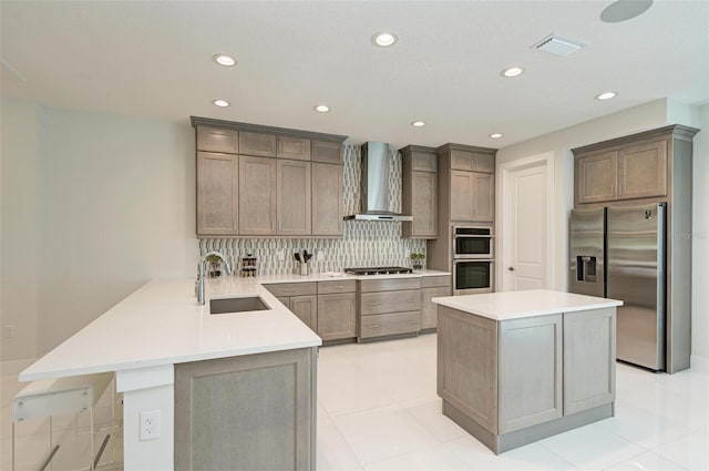 kitchen featuring light countertops, appliances with stainless steel finishes, a sink, a peninsula, and wall chimney exhaust hood