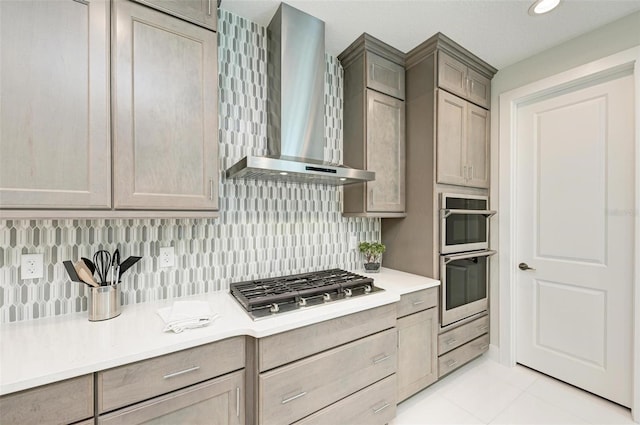 kitchen featuring light tile patterned floors, light countertops, appliances with stainless steel finishes, decorative backsplash, and wall chimney exhaust hood