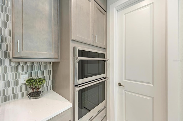 kitchen featuring stainless steel double oven, backsplash, and light stone countertops