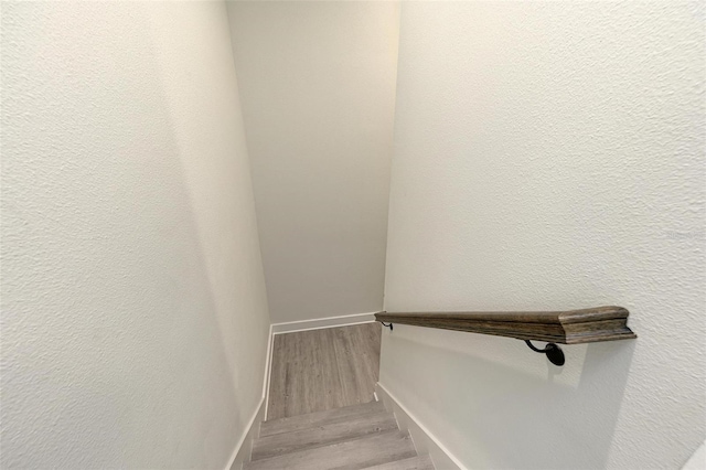 staircase with a textured wall, wood finished floors, and baseboards