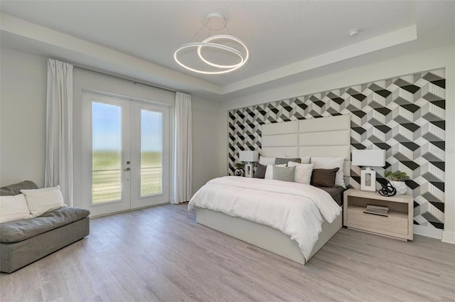 bedroom featuring light wood-style floors, access to outside, a tray ceiling, and french doors