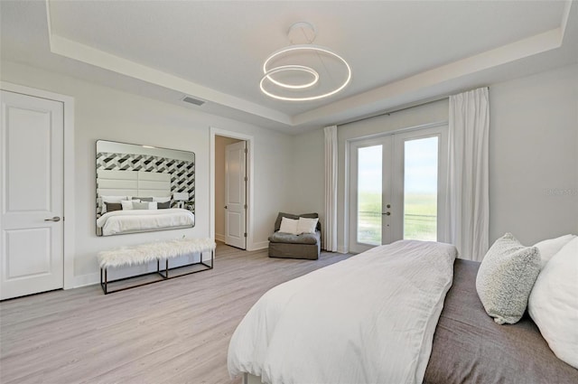 bedroom with access to exterior, a tray ceiling, french doors, light wood finished floors, and visible vents